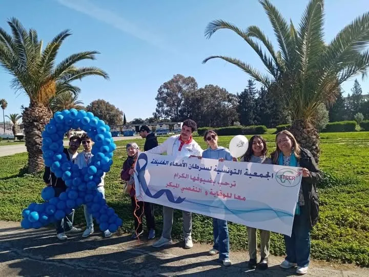 Bénévoles en plein air avec un grand ruban bleu en ballons et une banderole en arabe.